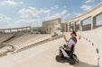 Person using a mobility device in an outdoor setting with architectural background.