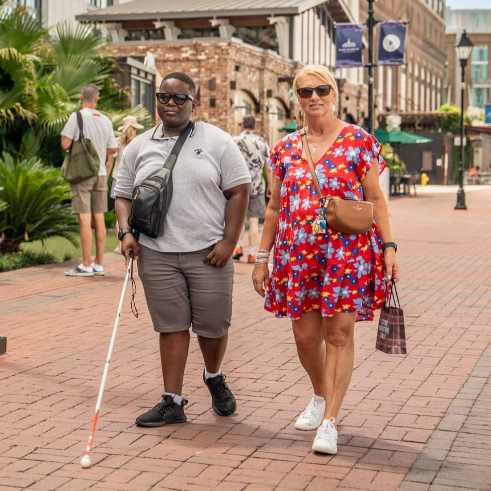 Two people walking on a city street, one with a walking stick, in an urban setting.
