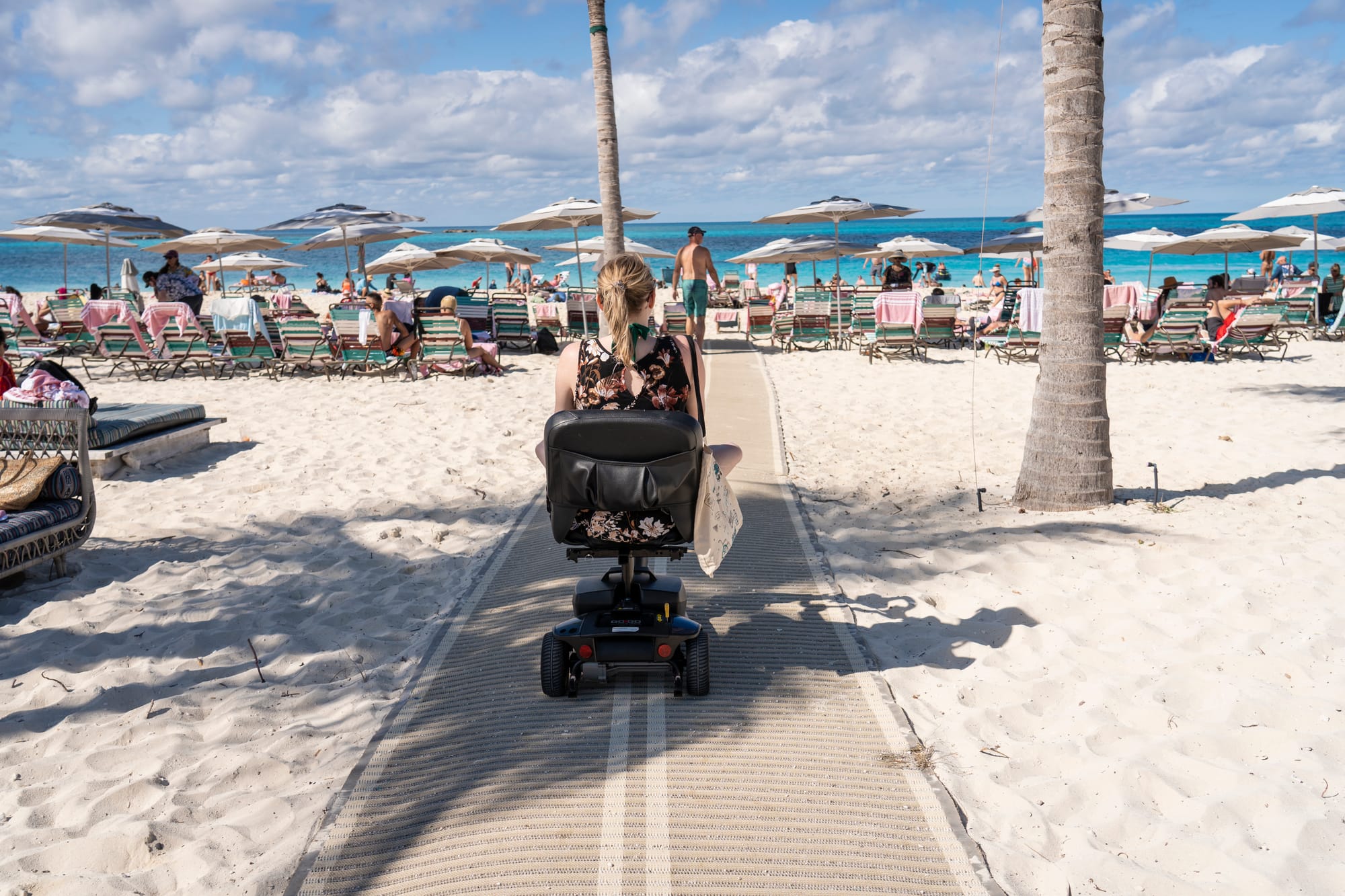 Person using a mobility scooter on a sandy beach with palm trees and umbrellas in the background