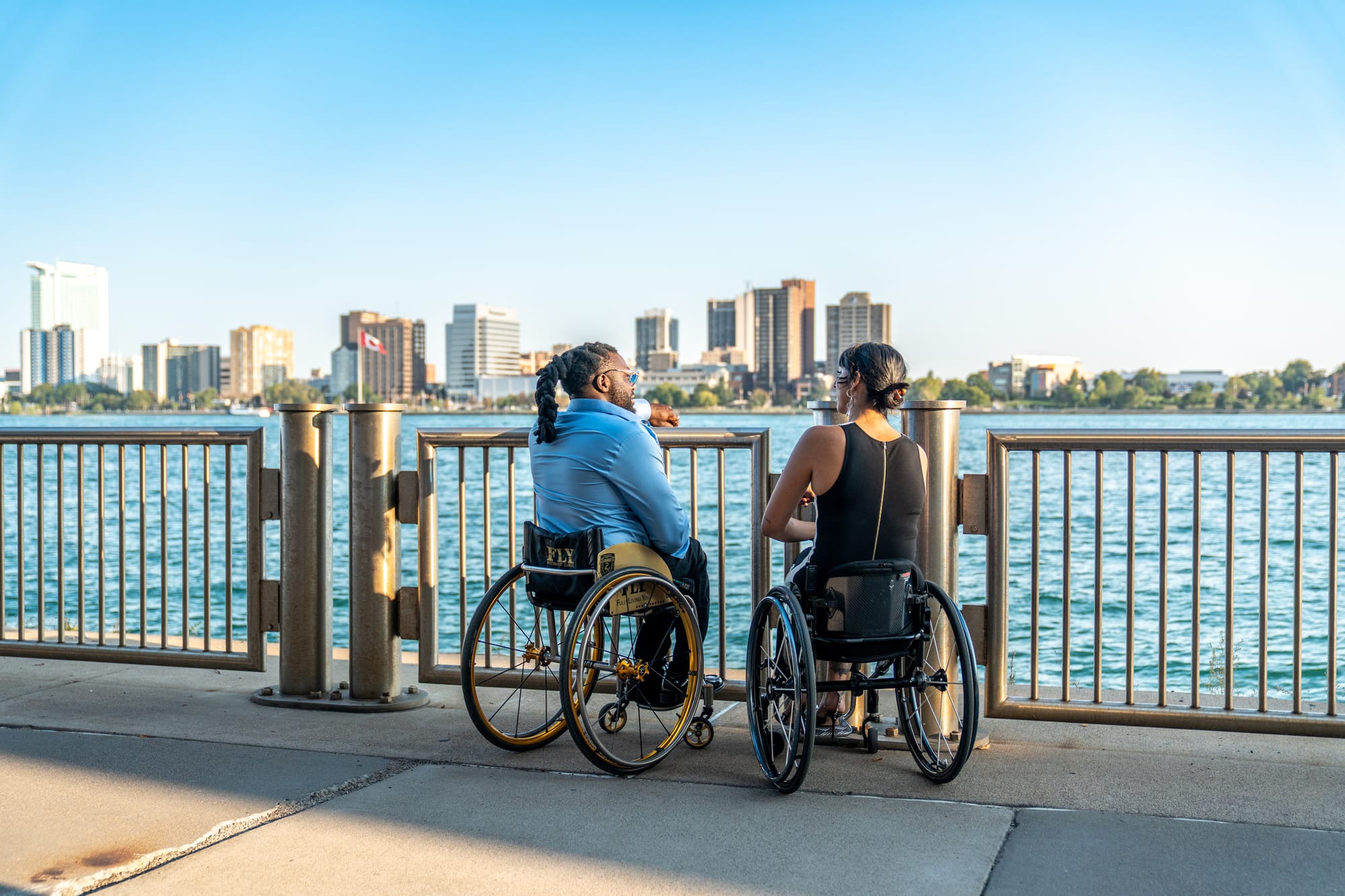 Two individuals using wheelchairs looking at a city skyline from a waterfront
