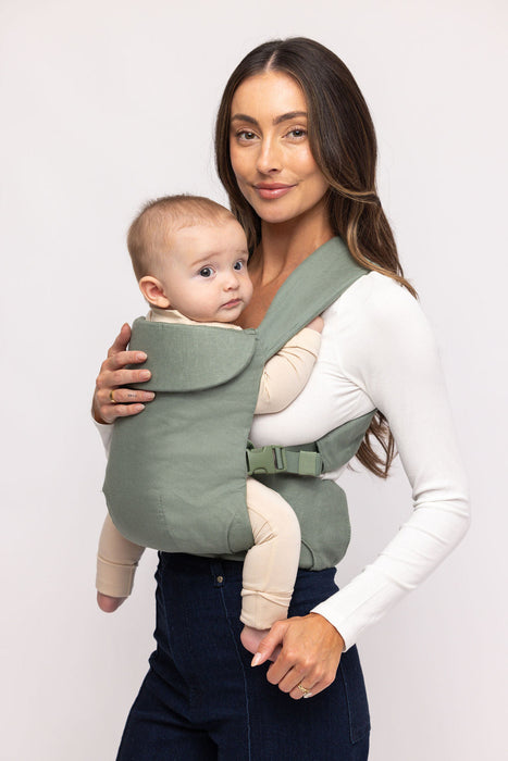 Woman holding a baby in a WildBird Acadian Aerial Buckle Baby Carrier on a white background