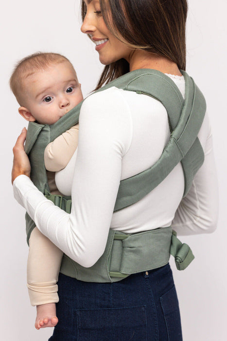 Back of woman holding a baby in a WildBird Acadian Aerial Buckle Baby Carrier on a white background