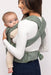 Back of woman holding a baby in a WildBird Acadian Aerial Buckle Baby Carrier on a white background