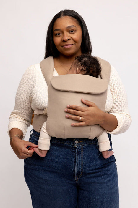 Woman holding a baby in a WildBird Desert Lark Aerial Buckle Baby Carrier on a white background