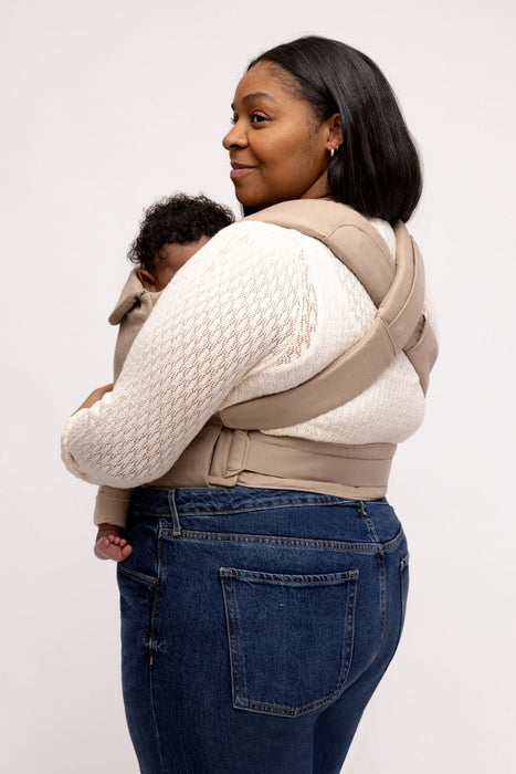 Back of woman holding a baby in a WildBird Desert Lark Aerial Buckle Baby Carrier on a white background
