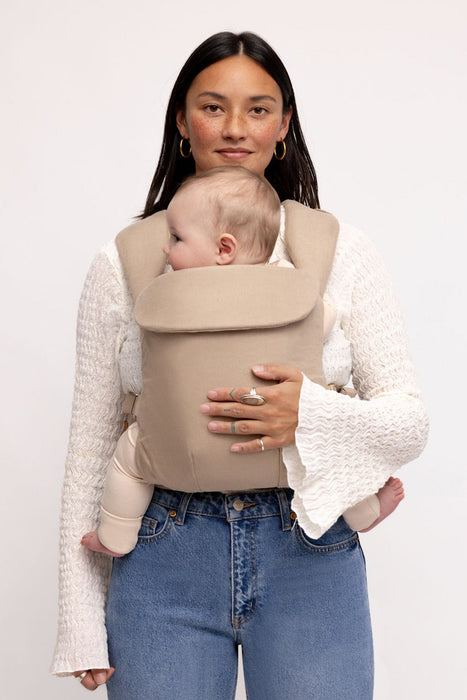 Woman holding a baby in a WildBird Desert Lark Aerial Buckle Baby Carrier on a white background