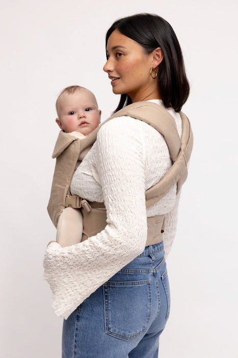 Back of woman holding a baby in a WildBird Desert Lark Aerial Buckle Baby Carrier on a white background