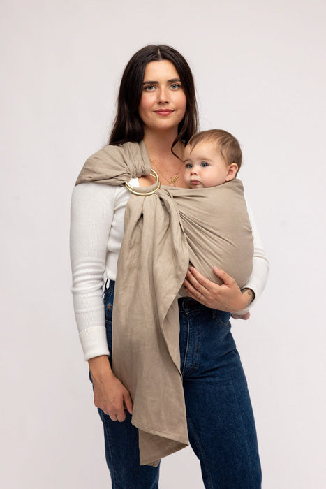 Woman holding a baby in a WildBird Desert Lark Linen Baby Sling on a white background