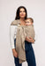Woman holding a baby in a WildBird Desert Lark Linen Baby Sling on a white background