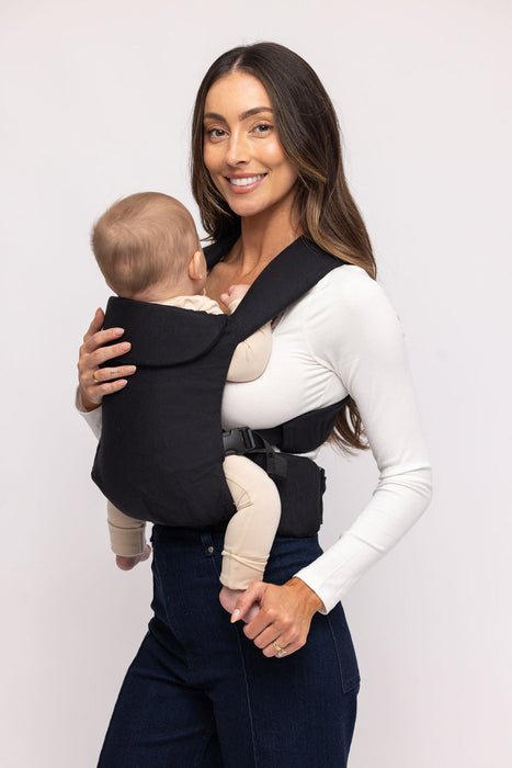 Woman holding a baby in a WildBird Raven Aerial Buckle Baby Carrier on a white background