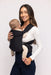 Woman holding a baby in a WildBird Raven Aerial Buckle Baby Carrier on a white background