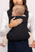 Detail of woman holding a baby in a WildBird Raven Aerial Buckle Baby Carrier on a white background