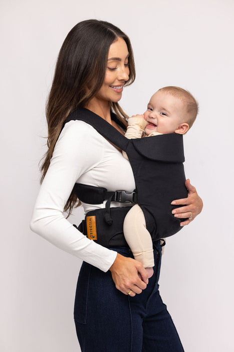Side of woman holding a baby in a WildBird Raven Aerial Buckle Baby Carrier on a white background