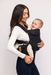 Side of woman holding a baby in a WildBird Raven Aerial Buckle Baby Carrier on a white background