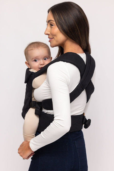 Back of woman holding a baby in a WildBird Raven Aerial Buckle Baby Carrier on a white background