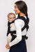 Back of woman holding a baby in a WildBird Raven Aerial Buckle Baby Carrier on a white background