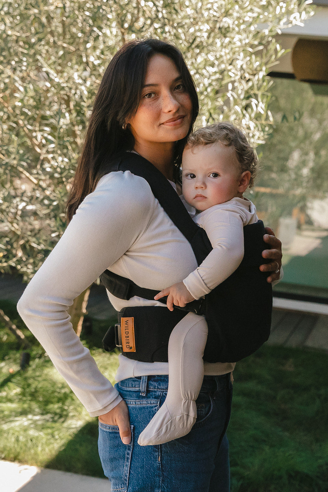 Woman holding a baby in a WildBird Raven Aerial Buckle Baby Carrier outdoors