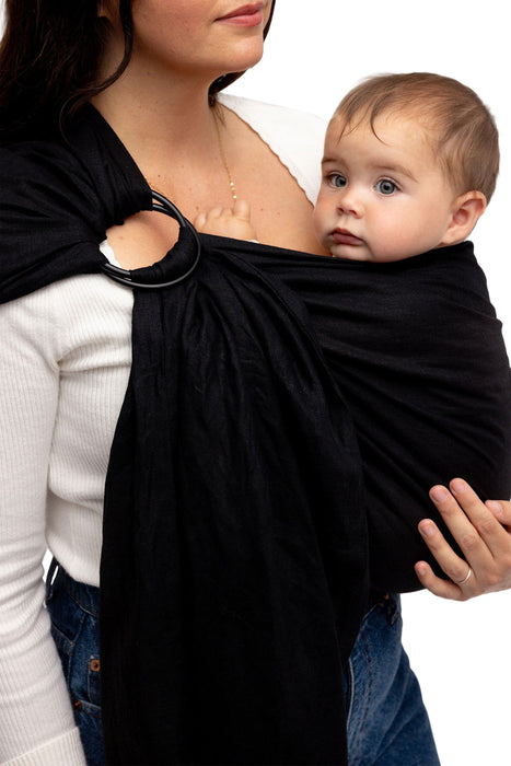 Front side detail of woman holding a baby in a WildBird Raven Linen Baby Sling on a white background