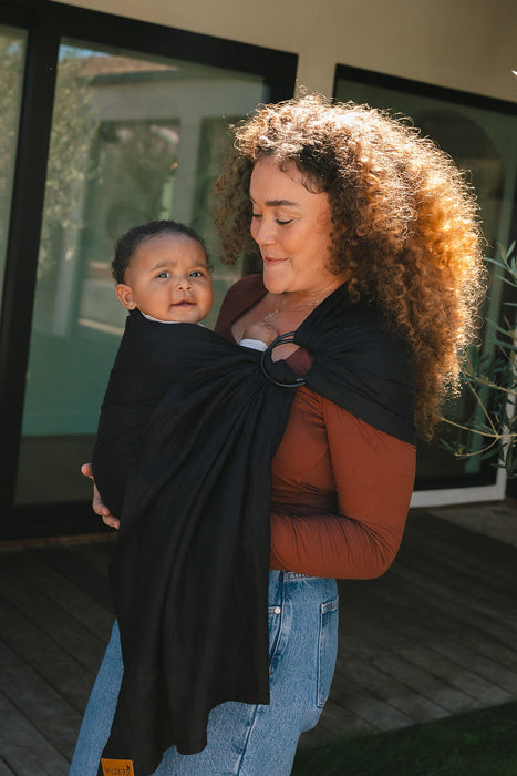 Woman holding a baby in a WildBird Raven Linen Baby Sling outdoors