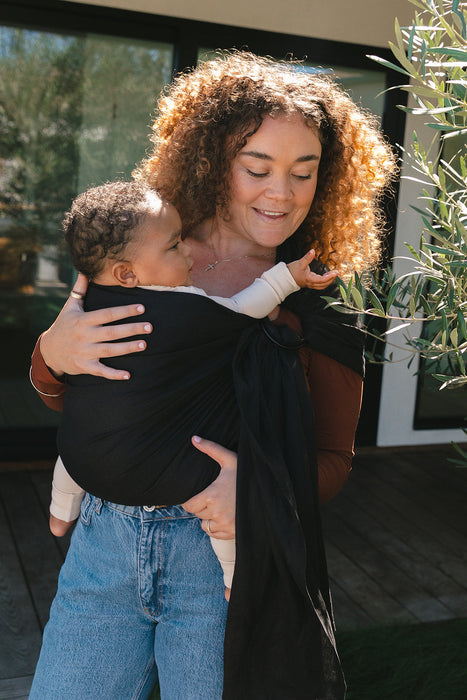 Woman holding a baby in a WildBird Raven Linen Baby Sling outdoors