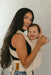 Woman holding a baby in a WildBird Sparrow Aerial Buckle Baby Carrier  against a plain background