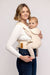 Side of woman holding a baby in a WildBird Sparrow Aerial Buckle Baby Carrier on a white background