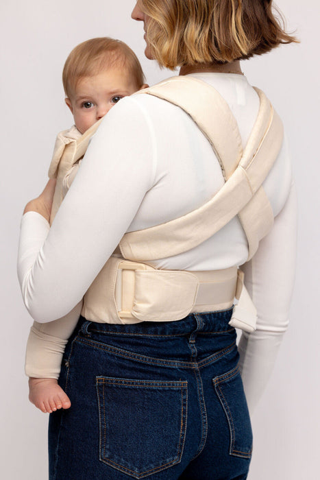 Back of woman holding a baby in a WildBird Sparrow Aerial Buckle Baby Carrier on a white background