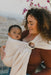 Woman holding a baby in a WildBird Sparrow Linen Baby Sling against a stone wall and floral background