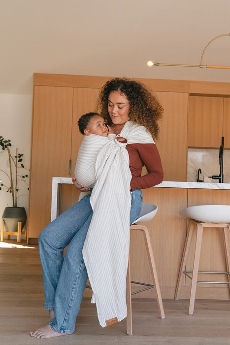 Woman holding a baby in a WildBird Swan Linen Baby Sling in a kitchen setting
