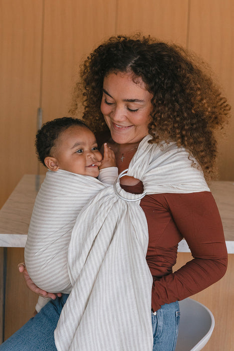Woman holding a baby in a WildBird Swan Linen Baby Sling against a wooden background