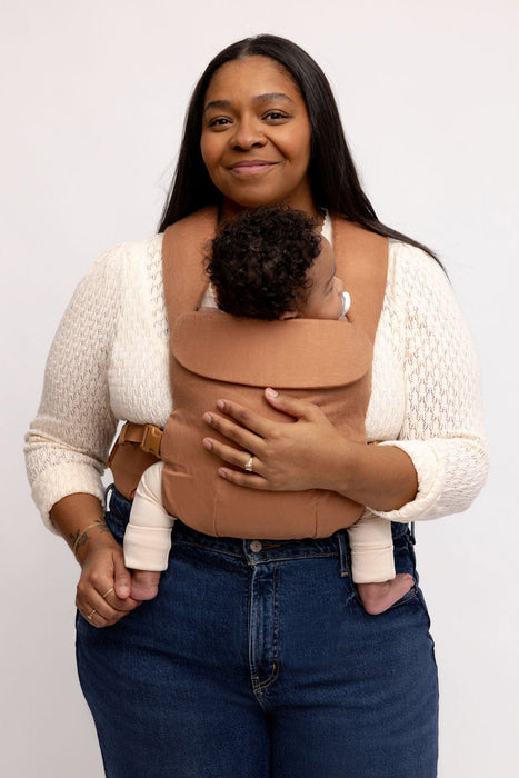 Woman holding a baby in a WildBird Willow Aerial Buckle Baby Carrier on a white background
