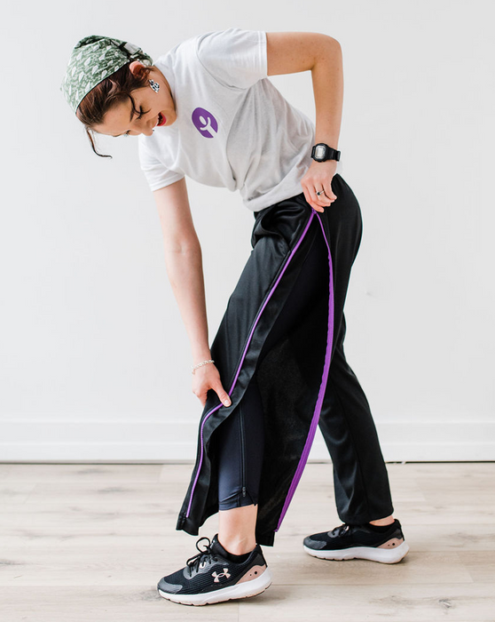 Woman unzipping the befree zipOns Adult Heavyweight Adaptive Pants against a white wall