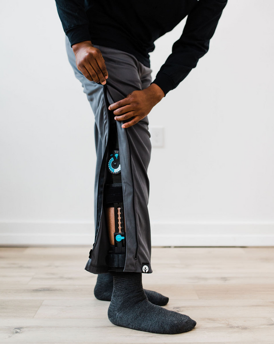 Man unzipping the befree zipOns Adult Heavyweight Adaptive Pants against a white wall
