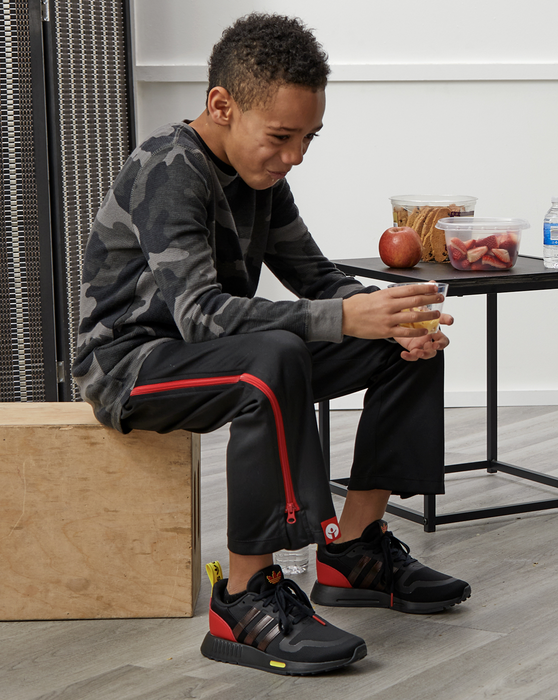 Child sitting on a box wearing the befree zipOns Youth Heavyweight Adaptive Pants with a table and snacks in the background
