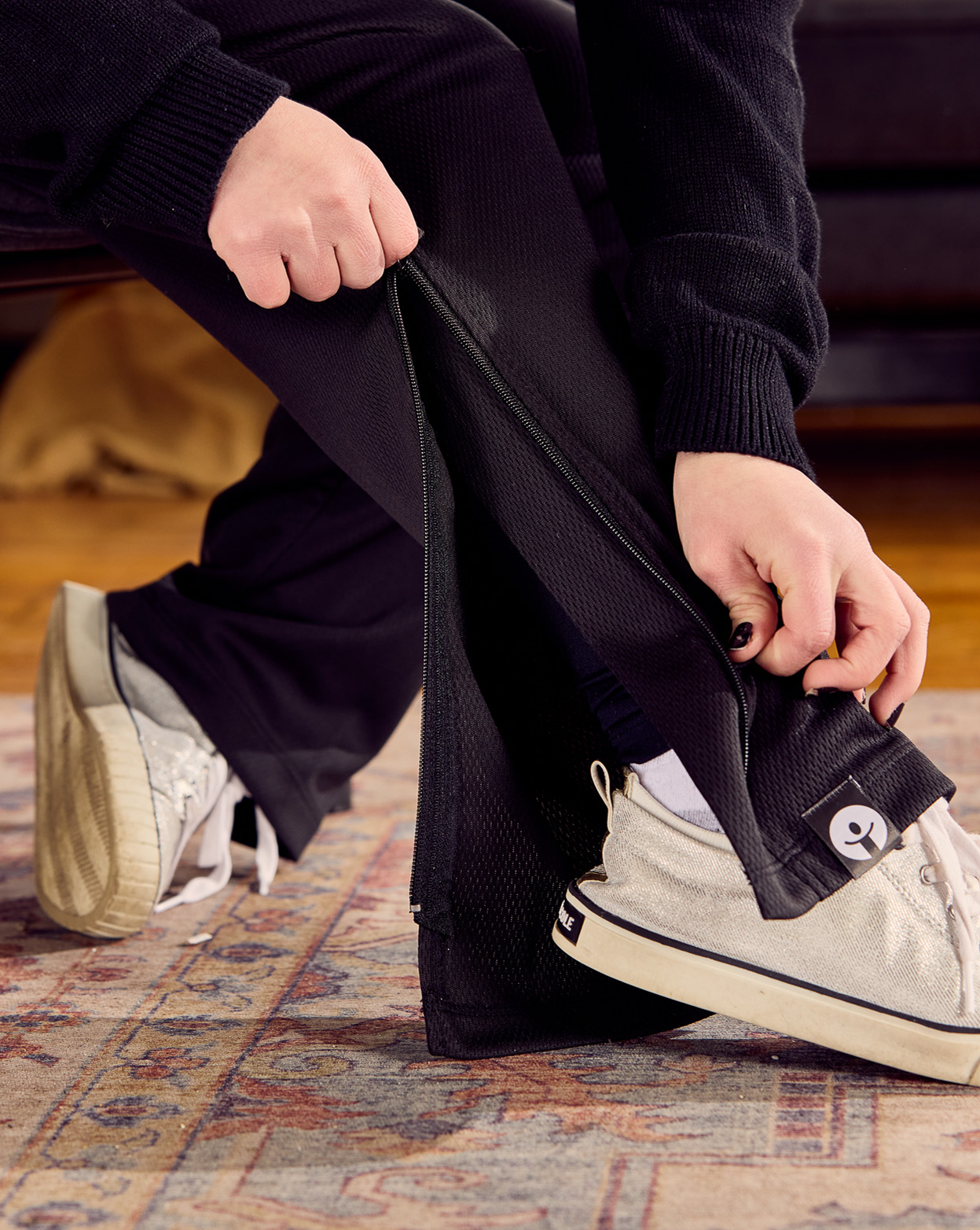 Person sitting on a patterned rug zipping up the befree zipOns Youth Lightweight Adaptive Pants 