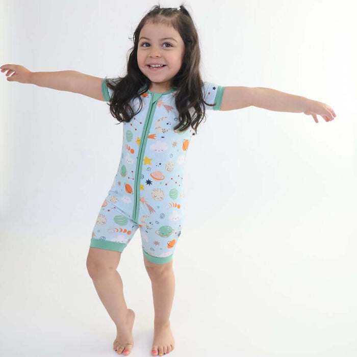 Young girl spreading her arms while wearing a Rainn Bamboo Cosmic Short Zipp Romper on a white background