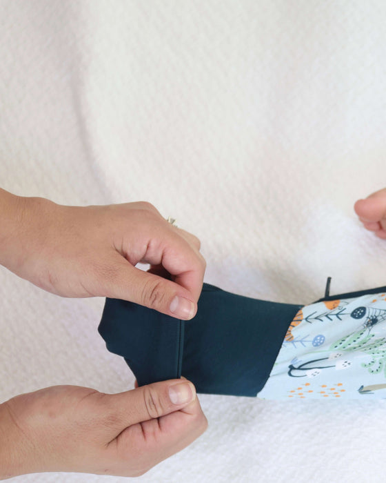 Detail of parent stretching the Rainn Bamboo Critter Hollow Zipp Jammies on a white background